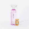 A clear spray bottle labeled Blueland Bathroom with pink liquid inside is next to a packet labeled Blueland Cleaner Tablet Eucalyptus Mint and a pink cleaning tablet on a white background.