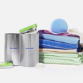 Two pastel-colored Blueland containers labeled “Oxi Laundry Booster” and “Laundry Detergent Tablets” next to laundry tablets, blue dryer balls, and a neatly folded stack of colorful towels.