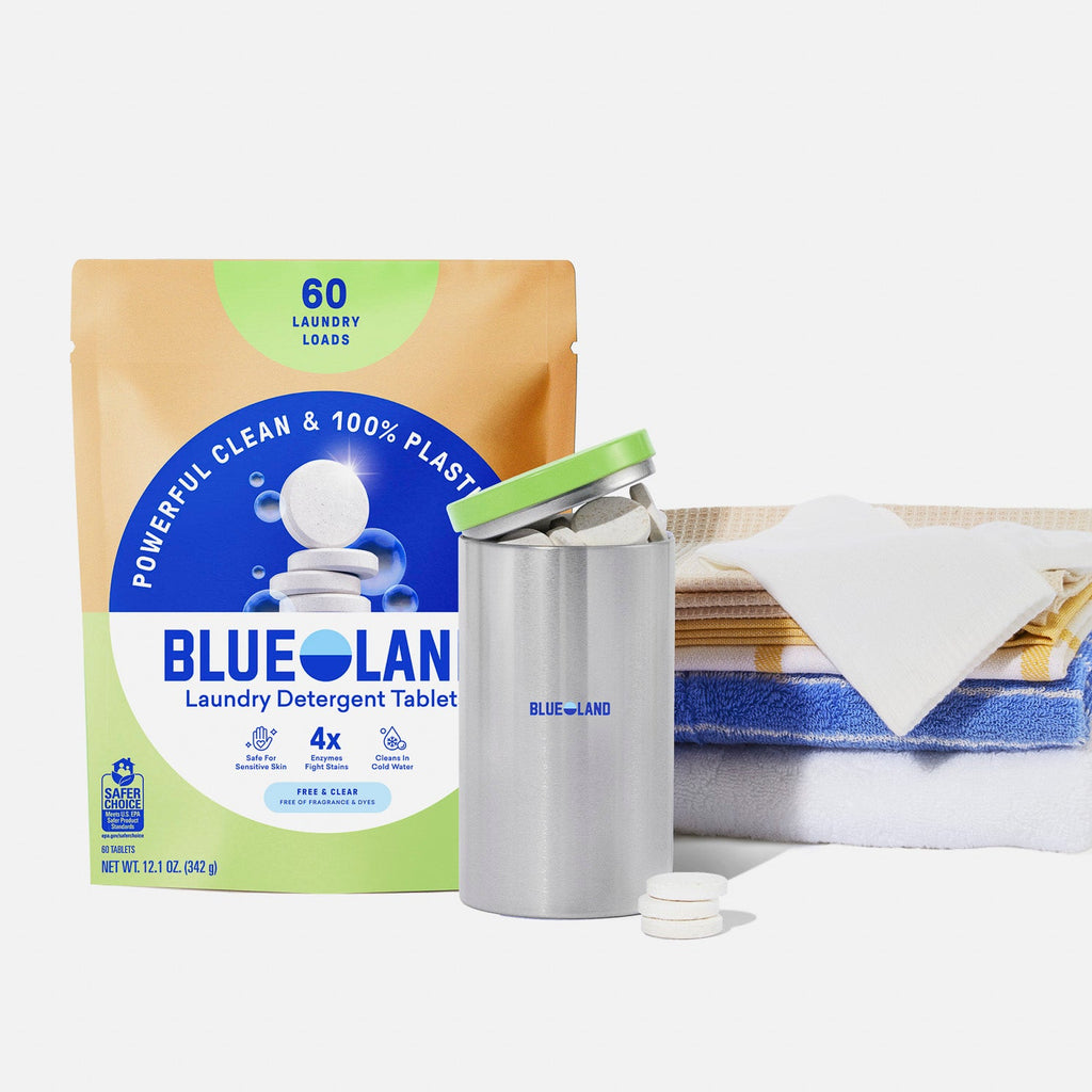 A package of Blueland laundry detergent tablets, a purple refillable container with tablets, and a neatly folded stack of towels with a cloth on top, displayed on a white background.