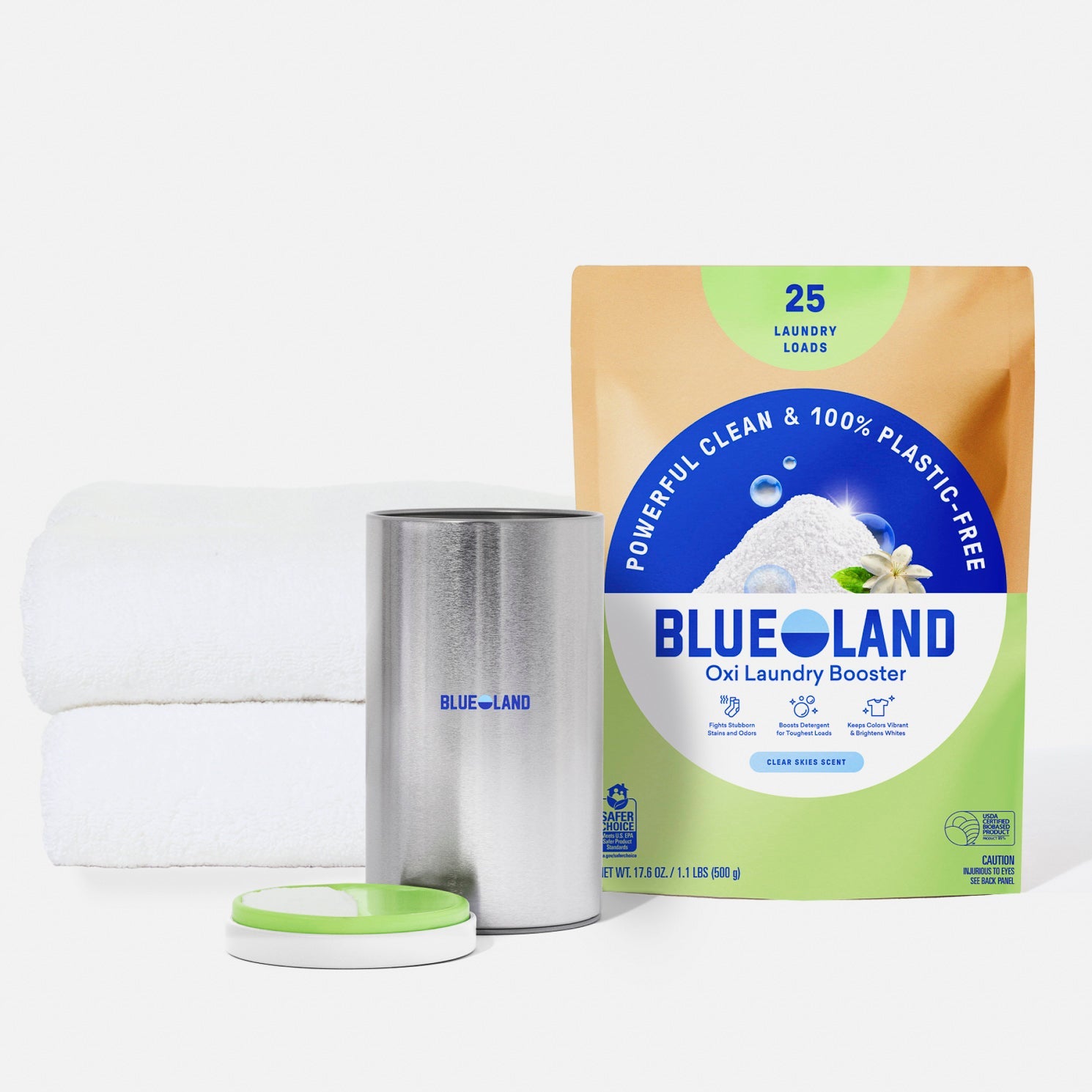 A package of Blueland Oxi Laundry Booster sits next to a pink canister with an open lid and two neatly folded white towels, all on a white background.