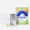 A package of Blueland Oxi Laundry Booster sits next to a pink canister with an open lid and two neatly folded white towels, all on a white background.