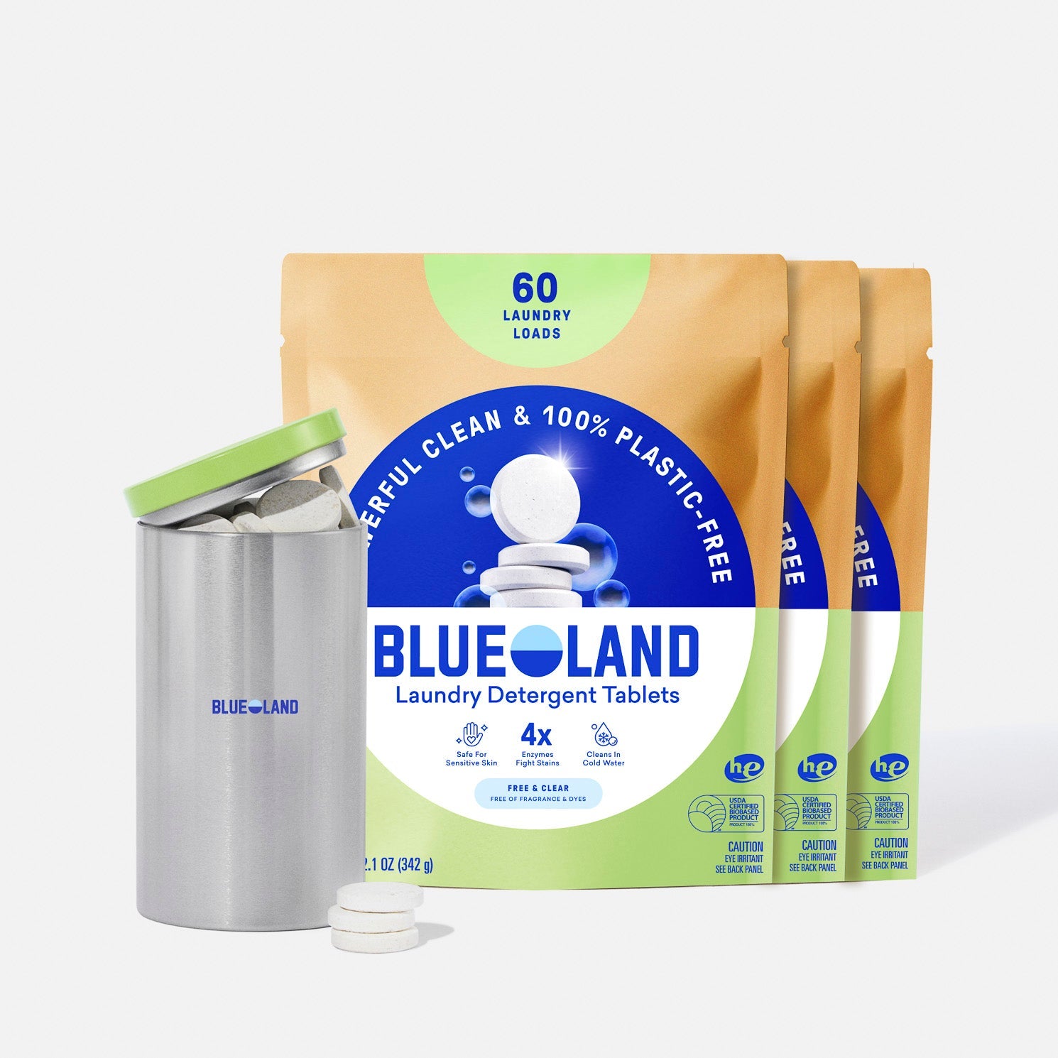 Three yellow and blue packages of Blueland Laundry Detergent Tablets stand upright behind a purple reusable tin with its lid off, displaying several white detergent tablets. The packaging highlights 60 laundry loads and plastic-free.