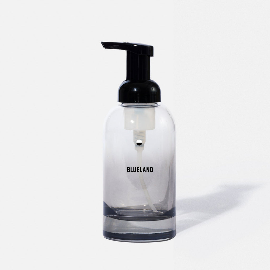 A clear glass soap dispenser with a black pump top and the word BLUELAND printed on the front, shown against a plain white background.